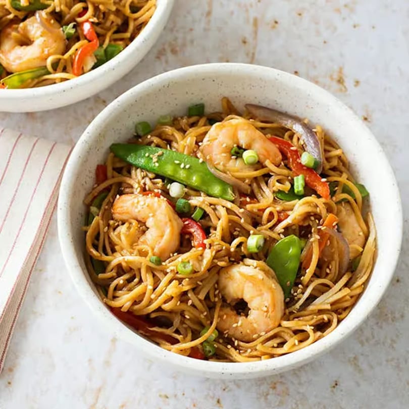 Two bowls of shrimp lo mein with snap peas, red peppers, and sesame seeds.