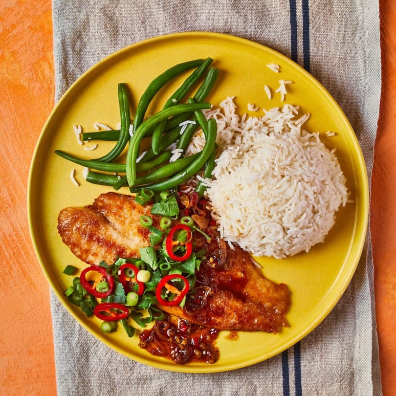 Pan-fried fish with chili sauce, green beans, and white rice on a yellow plate.