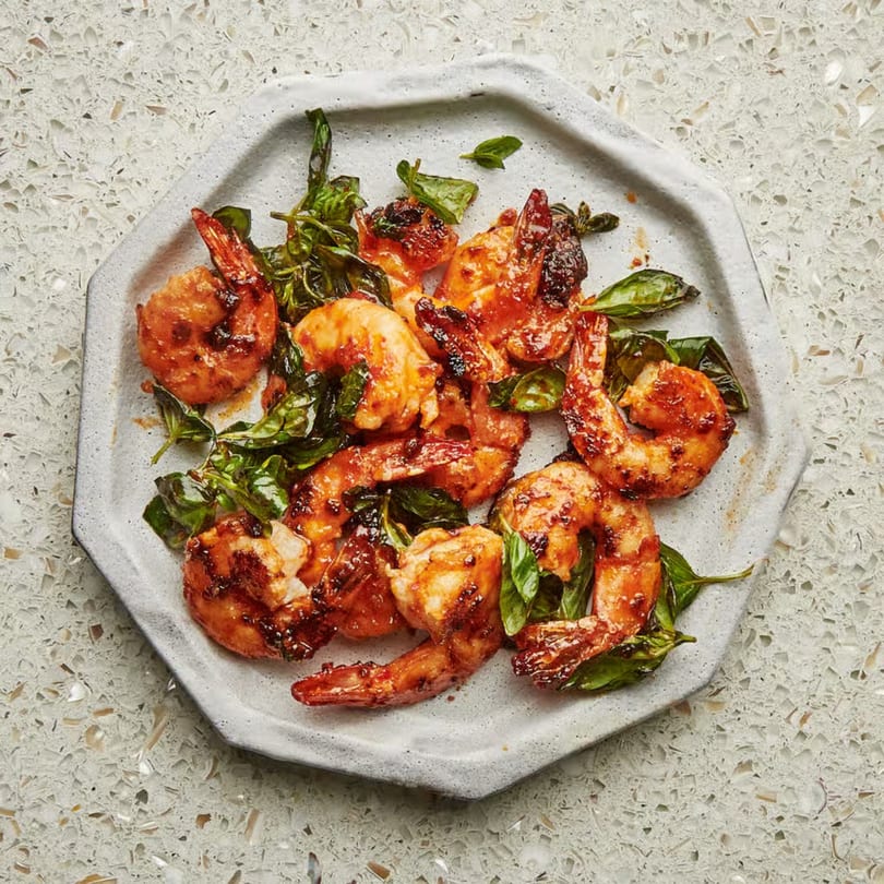 Spicy glazed shrimp with fresh basil leaves on a light gray octagonal plate.