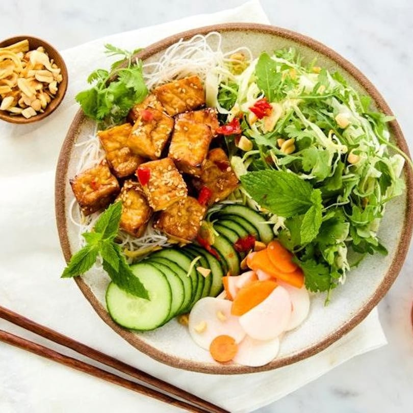 A colorful bowl of Vietnamese vermicelli noodles with crispy tofu, fresh herbs, and pickled vegetables.