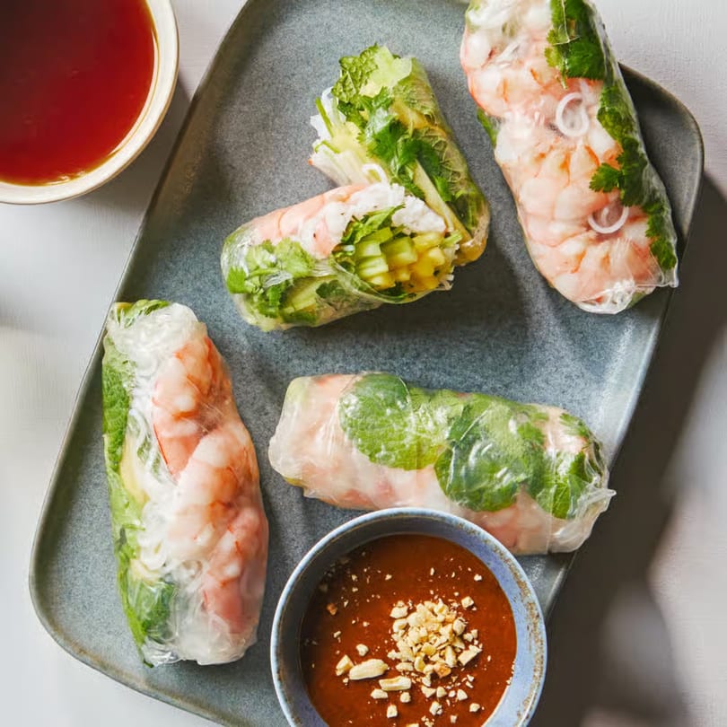 Four fresh shrimp spring rolls with herbs and vegetables, served with peanut and chili dipping sauces.